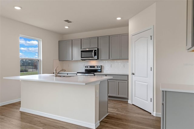 kitchen with gray cabinetry, a center island with sink, sink, appliances with stainless steel finishes, and wood-type flooring