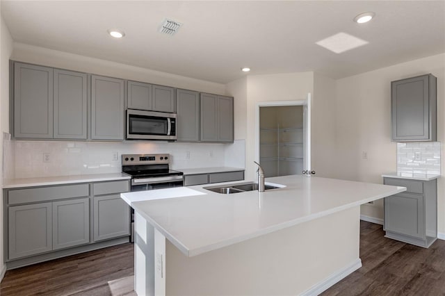 kitchen with an island with sink, stainless steel appliances, gray cabinetry, and sink