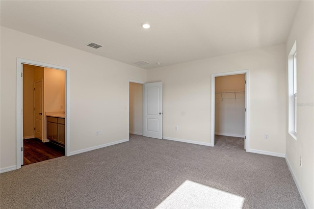 unfurnished bedroom featuring dark carpet, a spacious closet, connected bathroom, and a closet