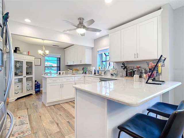 kitchen featuring light wood-style floors, white cabinetry, a sink, a peninsula, and ceiling fan with notable chandelier