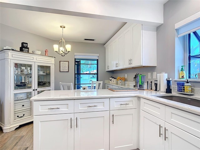 kitchen featuring light wood-style flooring, a peninsula, an inviting chandelier, light countertops, and white cabinetry