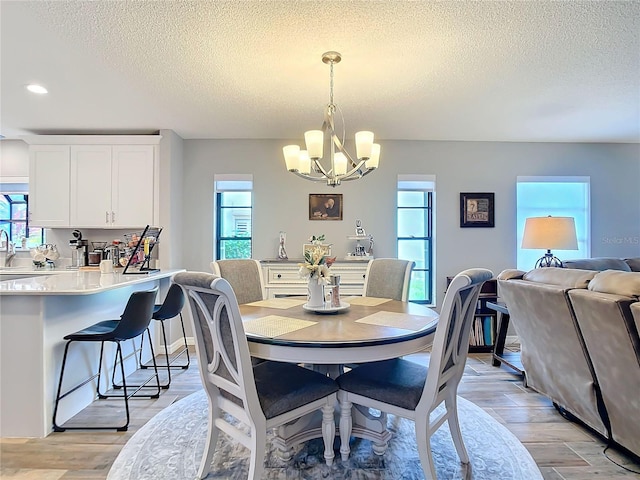 dining room featuring a chandelier, light wood finished floors, a textured ceiling, and a wealth of natural light