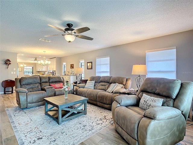 living area with ceiling fan with notable chandelier, light wood finished floors, a textured ceiling, and visible vents