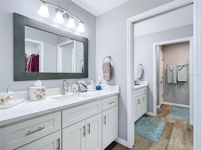 bathroom featuring a walk in closet, vanity, baseboards, and wood finished floors