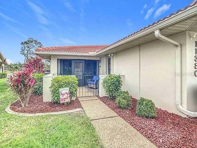 doorway to property featuring a lawn, a tile roof, and stucco siding