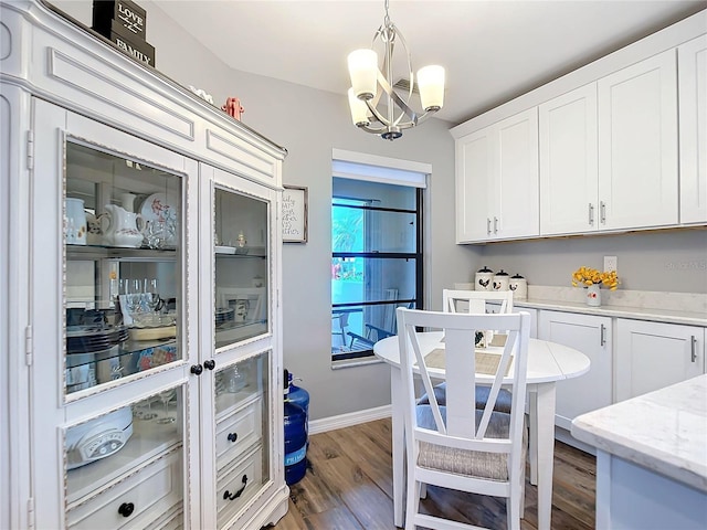 kitchen with dark wood finished floors, light stone counters, hanging light fixtures, an inviting chandelier, and white cabinetry