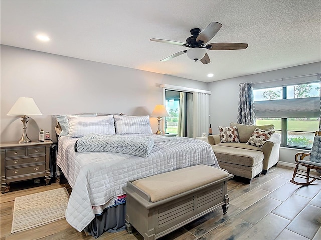 bedroom featuring a ceiling fan, multiple windows, a textured ceiling, and wood finished floors