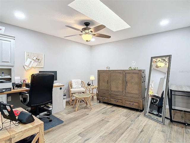 home office with light wood-type flooring, a skylight, and a ceiling fan