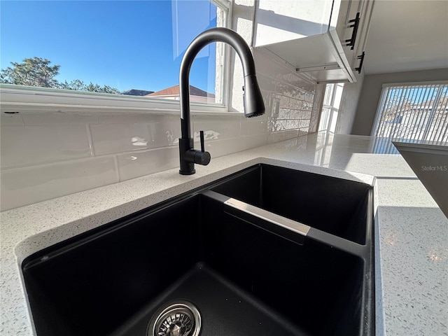 interior details with decorative backsplash, light stone countertops, and sink