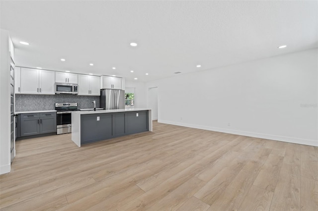 kitchen featuring gray cabinetry, an island with sink, tasteful backsplash, light hardwood / wood-style floors, and stainless steel appliances