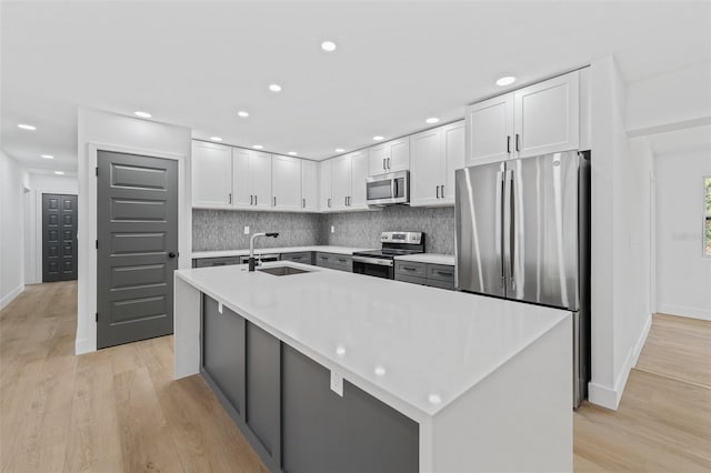 kitchen with white cabinets, sink, stainless steel appliances, and an island with sink