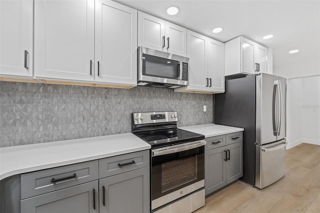 kitchen with white cabinets, gray cabinets, light wood-type flooring, appliances with stainless steel finishes, and tasteful backsplash