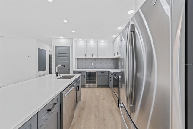 kitchen with appliances with stainless steel finishes, backsplash, beverage cooler, sink, and gray cabinets