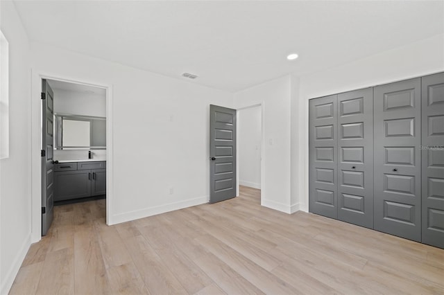 unfurnished bedroom featuring light hardwood / wood-style flooring, ensuite bath, and a closet