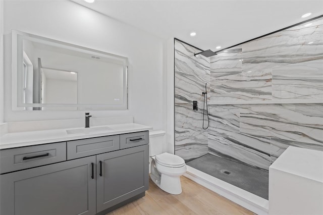 bathroom featuring hardwood / wood-style flooring, vanity, toilet, and tiled shower