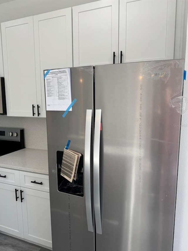 kitchen featuring white cabinets, stainless steel refrigerator with ice dispenser, and light stone countertops