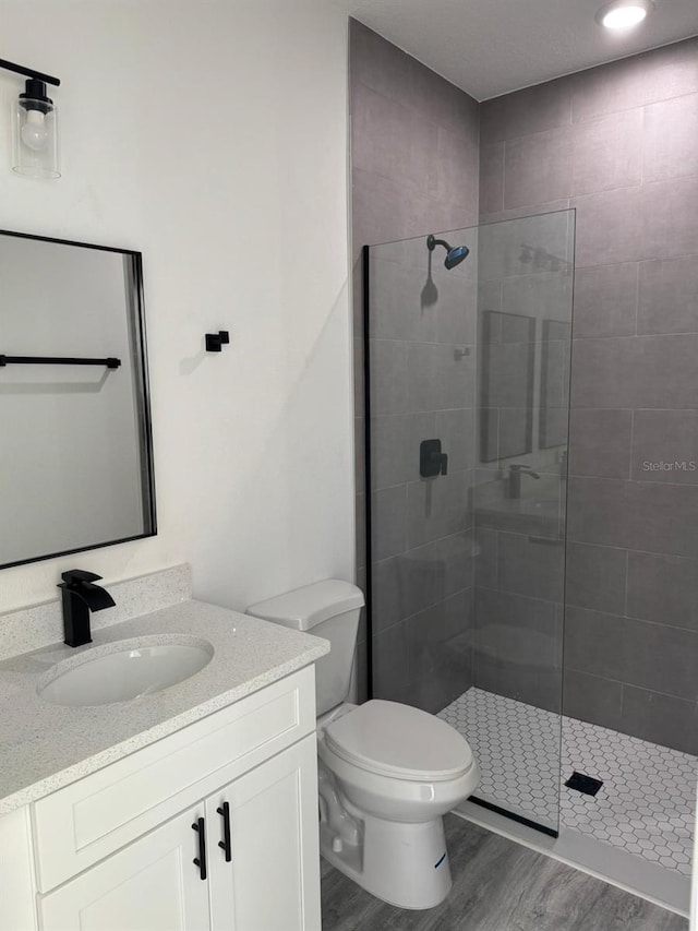 bathroom featuring toilet, vanity, a tile shower, and hardwood / wood-style floors