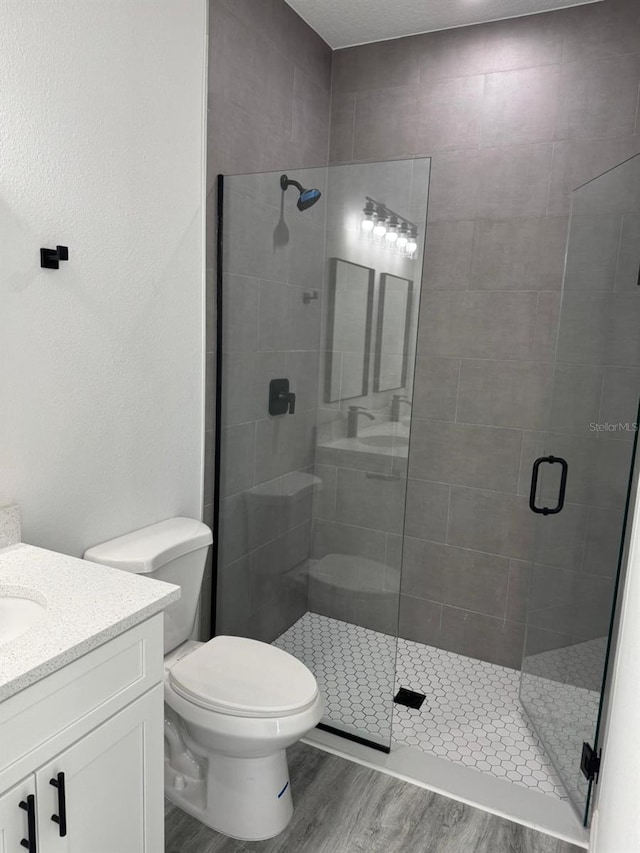 bathroom with toilet, vanity, a shower with door, and hardwood / wood-style flooring