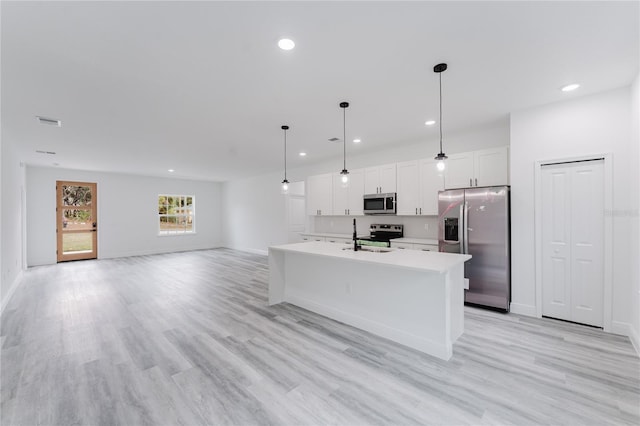 kitchen with appliances with stainless steel finishes, light hardwood / wood-style flooring, pendant lighting, white cabinetry, and a kitchen island with sink