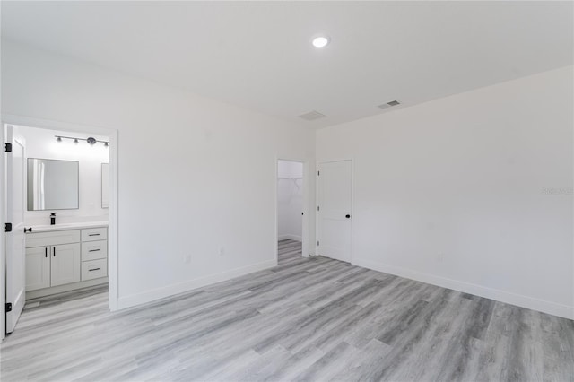 unfurnished bedroom featuring light hardwood / wood-style flooring, a closet, a spacious closet, ensuite bath, and sink