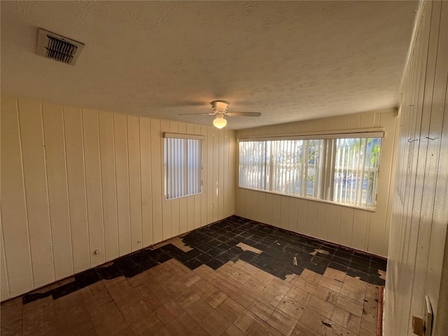 empty room with a textured ceiling, ceiling fan, and wooden walls