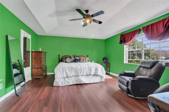 bedroom featuring a tray ceiling, ceiling fan, dark hardwood / wood-style flooring, and a textured ceiling