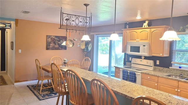 kitchen with light brown cabinets, white appliances, hanging light fixtures, and light tile patterned flooring