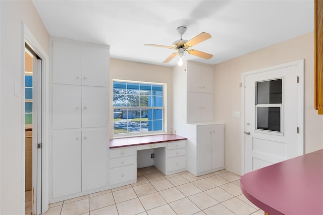 interior space with white cabinets, ceiling fan, built in desk, and light tile patterned floors