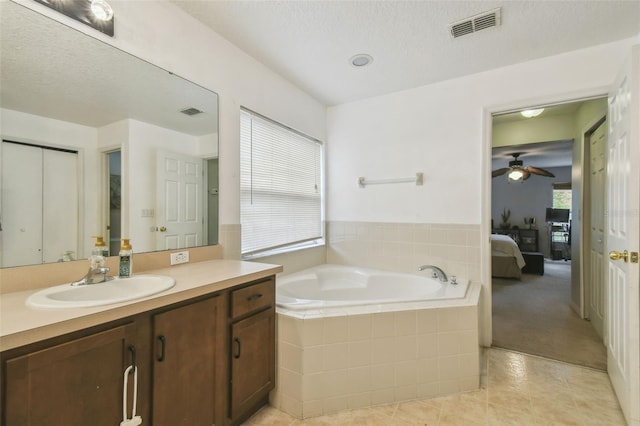 bathroom with a textured ceiling, tiled tub, tile patterned floors, vanity, and ceiling fan