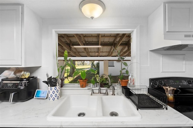 kitchen with black range with electric stovetop, sink, light stone counters, range hood, and white cabinets