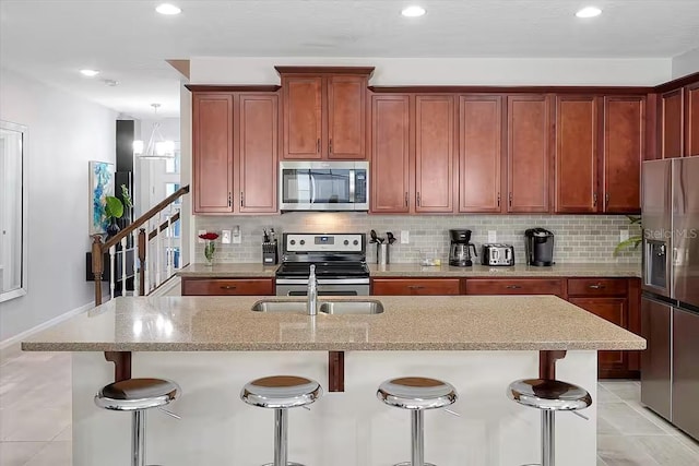 kitchen featuring backsplash, a center island with sink, a kitchen breakfast bar, light stone counters, and stainless steel appliances