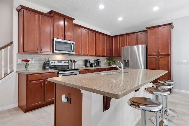 kitchen with a center island with sink, a kitchen bar, sink, and appliances with stainless steel finishes