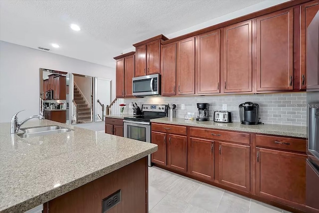 kitchen featuring decorative backsplash, appliances with stainless steel finishes, light stone counters, a textured ceiling, and sink