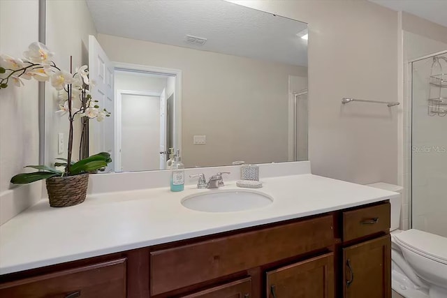 bathroom with a shower with door, vanity, a textured ceiling, and toilet