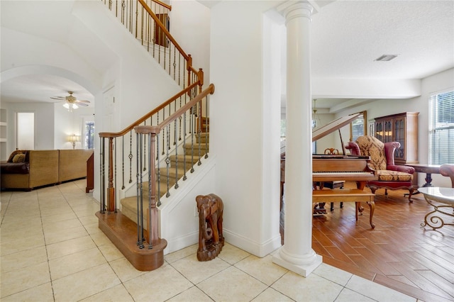 stairs featuring tile patterned flooring, ceiling fan, ornate columns, and a textured ceiling