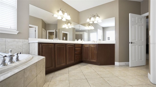 bathroom with tile patterned flooring, vanity, tiled tub, and an inviting chandelier