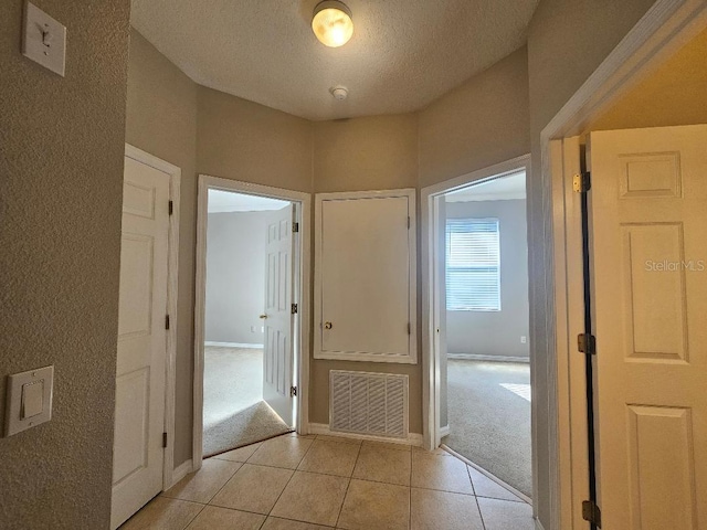 hall with a textured ceiling and light tile patterned flooring