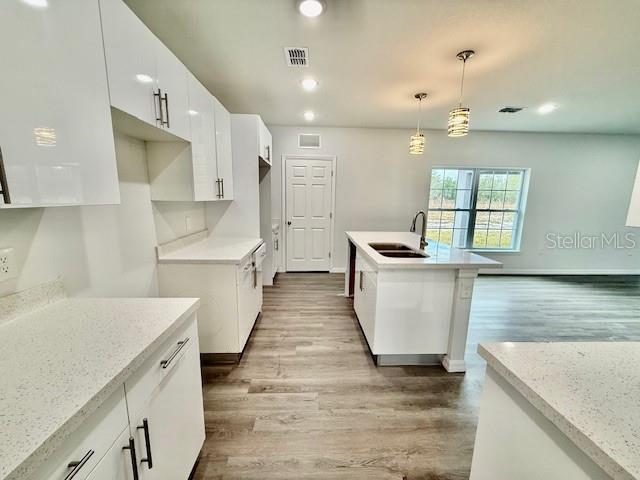 kitchen with light stone counters, decorative light fixtures, white cabinetry, and sink