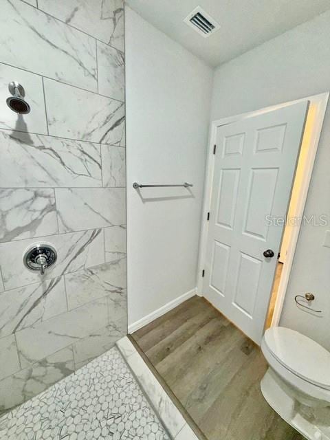 bathroom featuring a tile shower, hardwood / wood-style flooring, and toilet