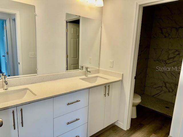 bathroom with hardwood / wood-style flooring, vanity, toilet, and a tile shower