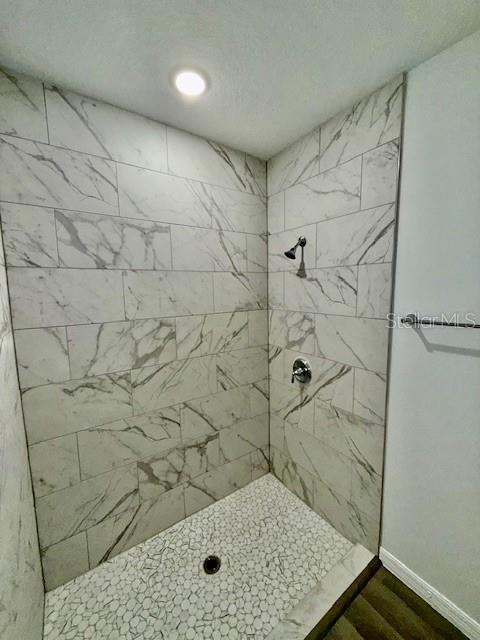 bathroom with a tile shower and wood-type flooring