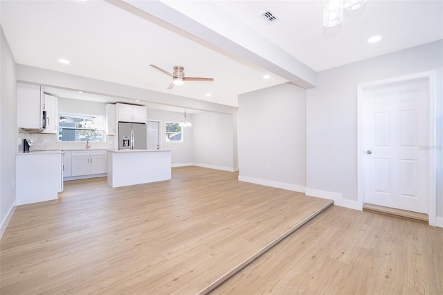 unfurnished living room with ceiling fan, beam ceiling, light wood-type flooring, and sink