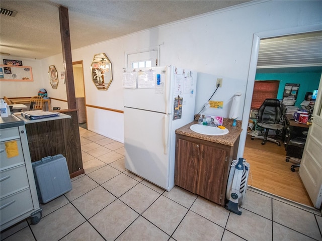 kitchen with a textured ceiling, white fridge, light tile patterned floors, and sink