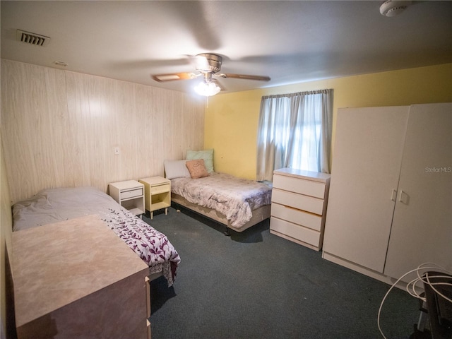 carpeted bedroom with ceiling fan and wood walls