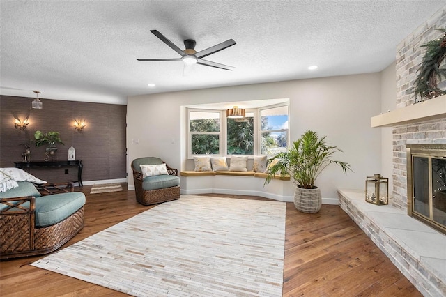 living room with a textured ceiling, hardwood / wood-style flooring, a brick fireplace, and ceiling fan