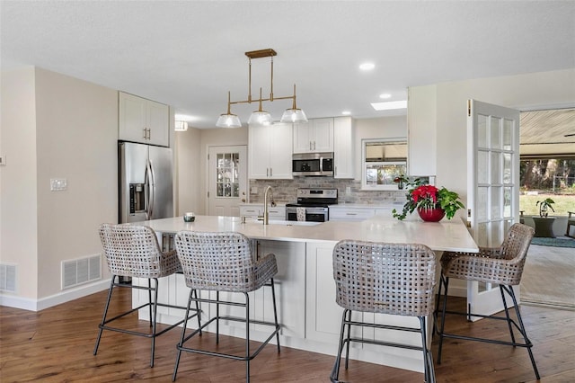 kitchen with hanging light fixtures, white cabinetry, stainless steel appliances, and a breakfast bar area