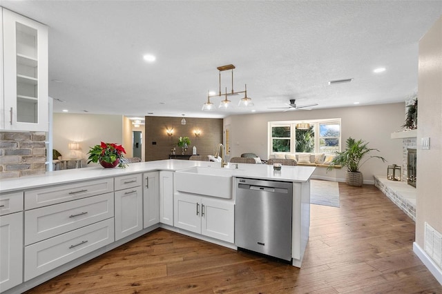 kitchen with kitchen peninsula, stainless steel dishwasher, a fireplace, sink, and white cabinets