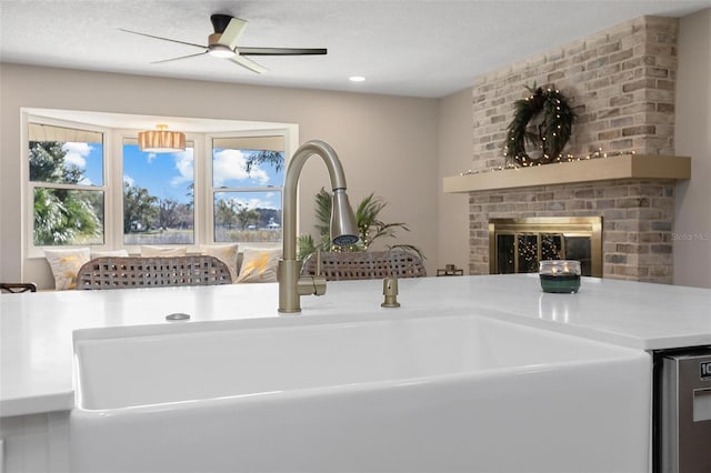 interior space featuring sink, a brick fireplace, stainless steel dishwasher, ceiling fan, and a textured ceiling