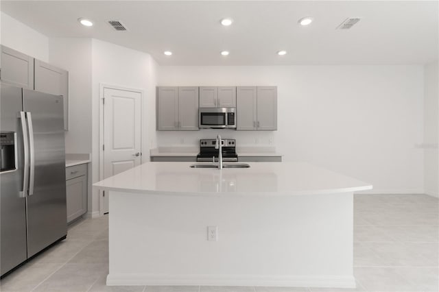 kitchen featuring gray cabinetry, light tile patterned flooring, stainless steel appliances, and an island with sink