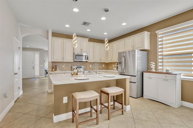 kitchen featuring stainless steel appliances, a breakfast bar area, decorative backsplash, a center island with sink, and light tile patterned floors